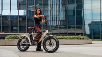 Mujer de pie junto a la bicicleta eléctrica plegable fat bike OneSport OT16 Max en color beige en la ciudad