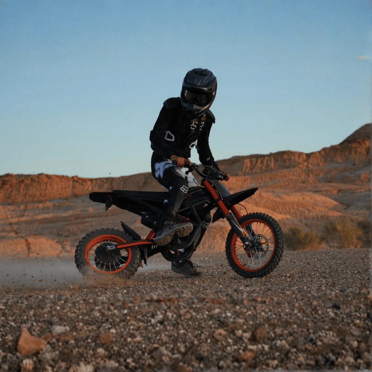Piloto con la moto cross eléctrica Ridingtimes GT54 fuera de pista sobre terreno arenoso al atardecer