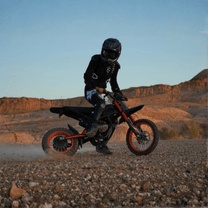 Piloto con la moto cross eléctrica Ridingtimes GT54 fuera de pista sobre terreno arenoso al atardecer