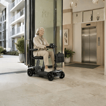 Mujer mayor sentada en el scooter de movilidad Sweetrich Air Traveller en interior