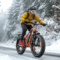 Hombre montando la bicicleta eléctrica fat bike VARUN M26-2 Plus en color naranja con casco en la nieve