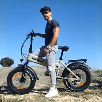 Hombre de pie junto a la bicicleta eléctrica plegable fat bike VARUN S20-1 en color beige sobre el césped