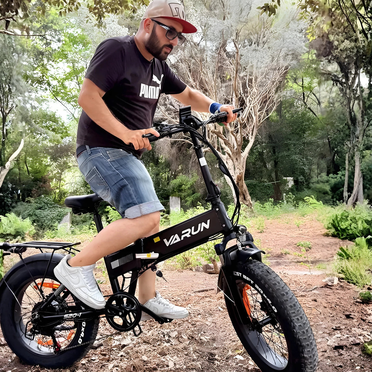 Hombre montando la bicicleta eléctrica plegable fat bike VARUN S20-1 en color negro en el bosque