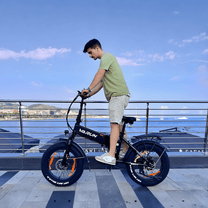 Hombre montando la bicicleta eléctrica plegable fat bike VARUN S20-1 en color negro junto al mar