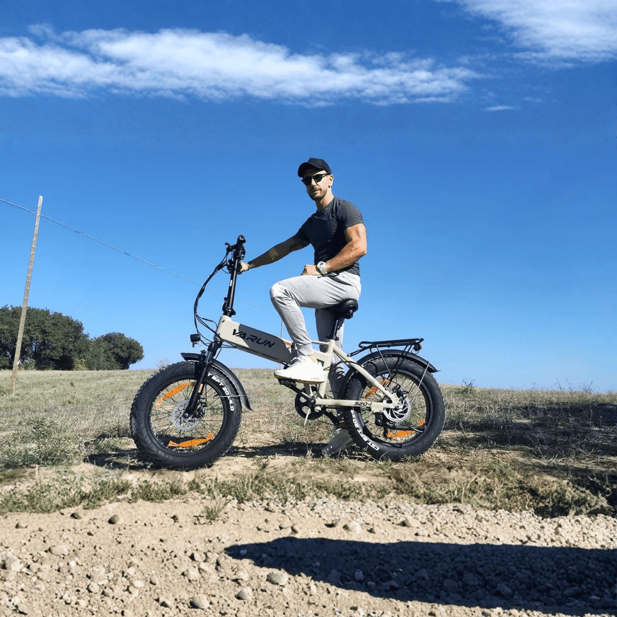 Hombre montando la bicicleta eléctrica plegable fat bike VARUN S20-1 en color beige por un camino de grava