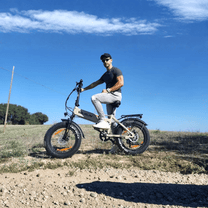 Hombre montando la bicicleta eléctrica plegable fat bike VARUN S20-1 en color beige por un camino de grava