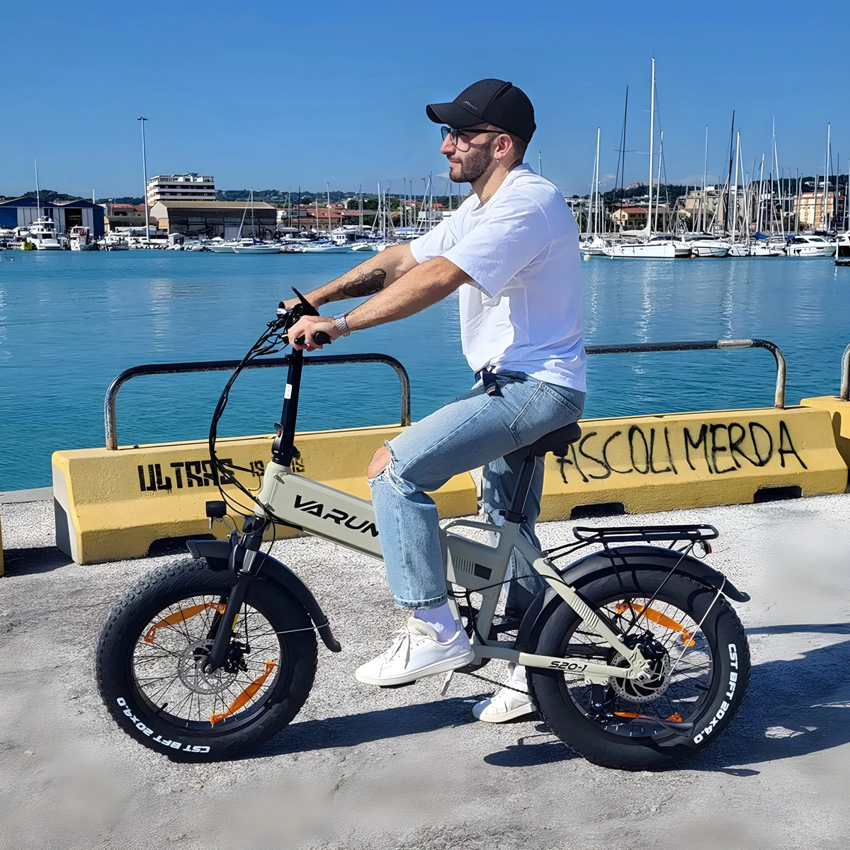 Hombre sentado en la bicicleta eléctrica plegable fat bike VARUN S20-1 en color beige junto al mar