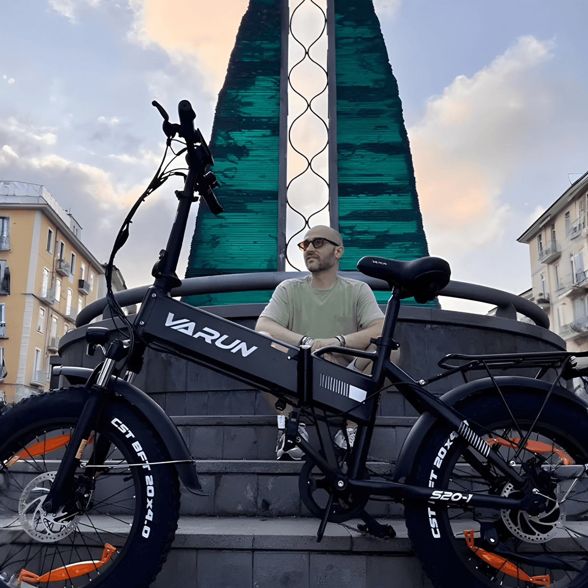 Hombre de pie junto a la bicicleta eléctrica plegable fat bike VARUN S20-1 en color negro en la ciudad