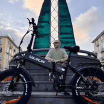 Hombre de pie junto a la bicicleta eléctrica plegable fat bike VARUN S20-1 en color negro en la ciudad