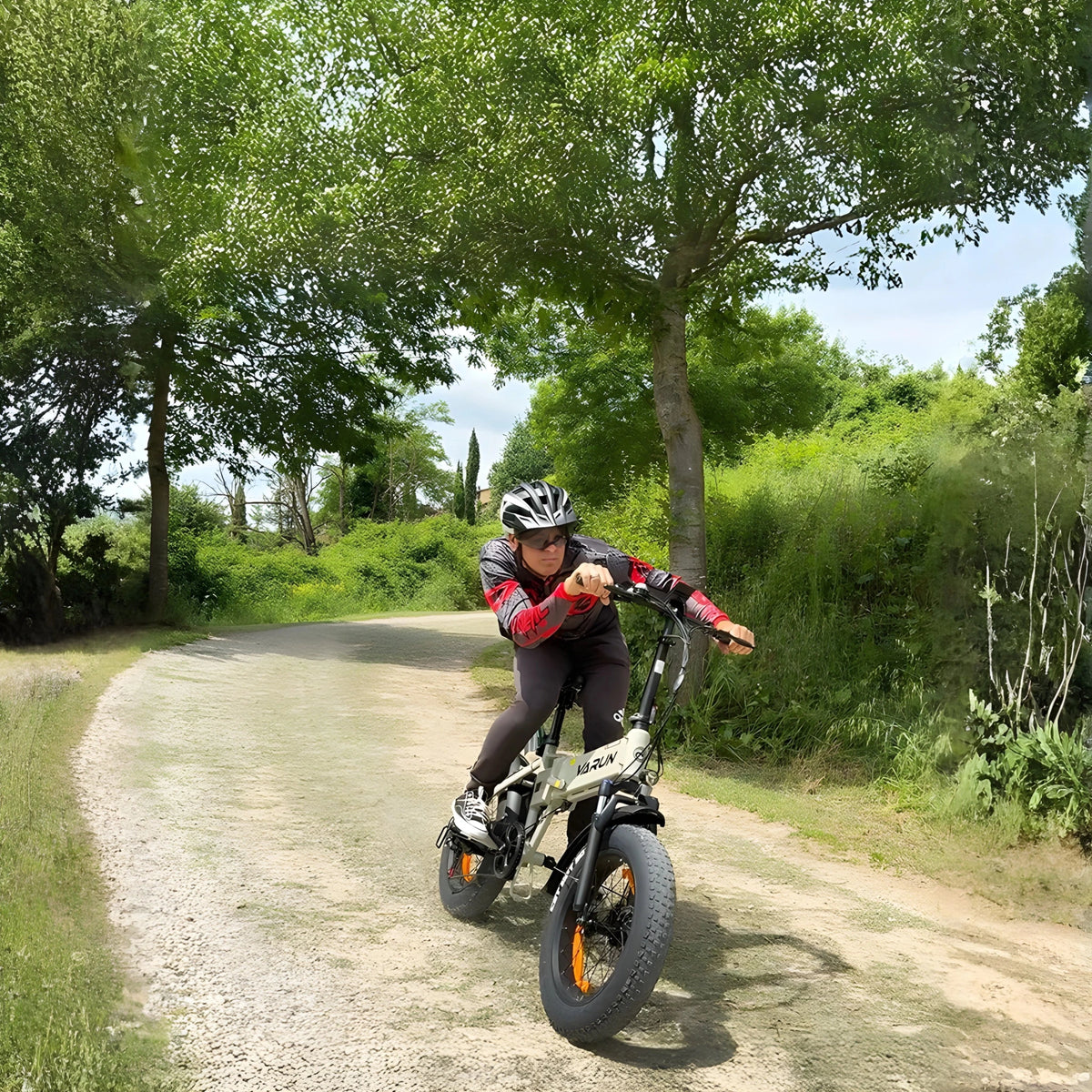 Hombre montando la bicicleta eléctrica plegable fat bike VARUN S20-1 en color beige con casco por un camino peatonal
