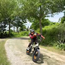 Hombre montando la bicicleta eléctrica plegable fat bike VARUN S20-1 en color beige con casco por un camino peatonal