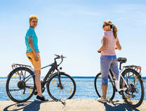 Dos personas con la bicicleta eléctrica VARUN S700-1 junto al mar